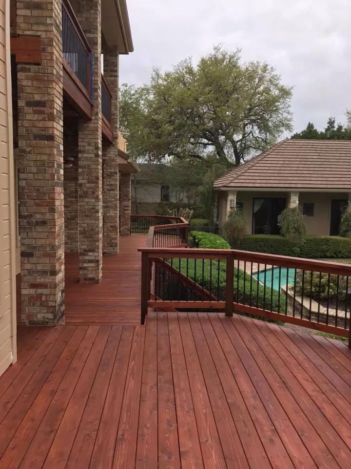 Wraparound stained deck overlooking a neighboring pool and stone columned guest house