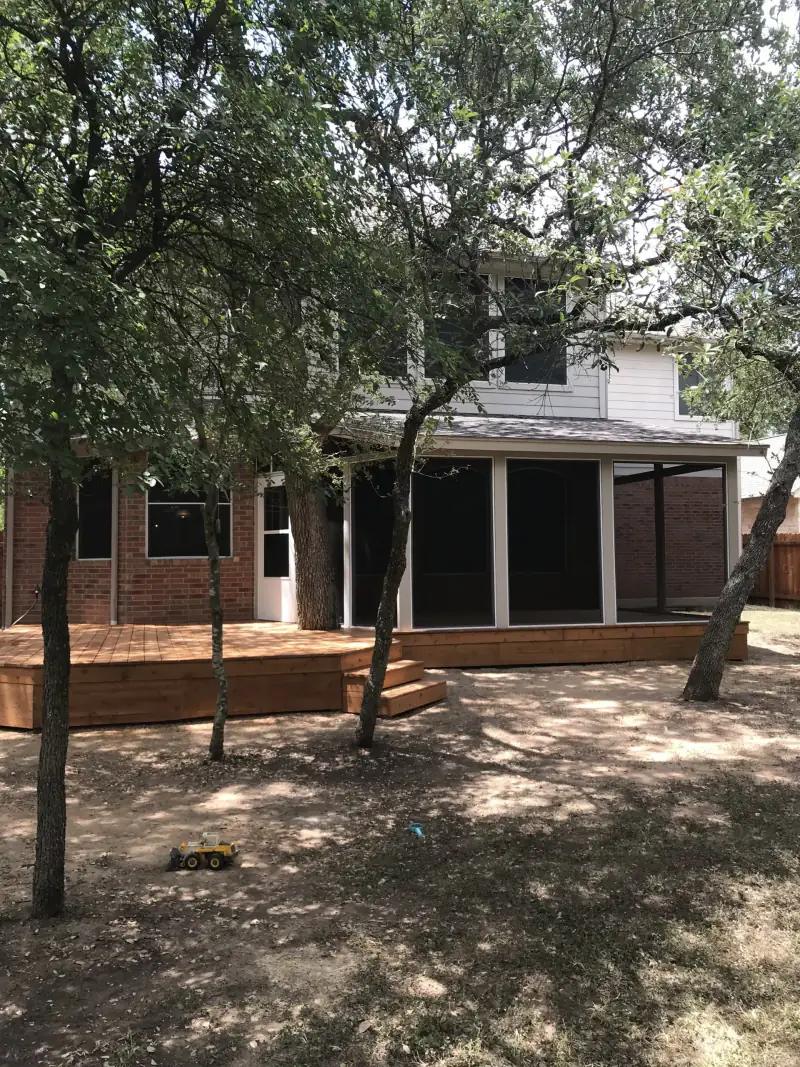 Large stained wood deck and adjoining screened porch on a two story brick home shaded by mature oaks
