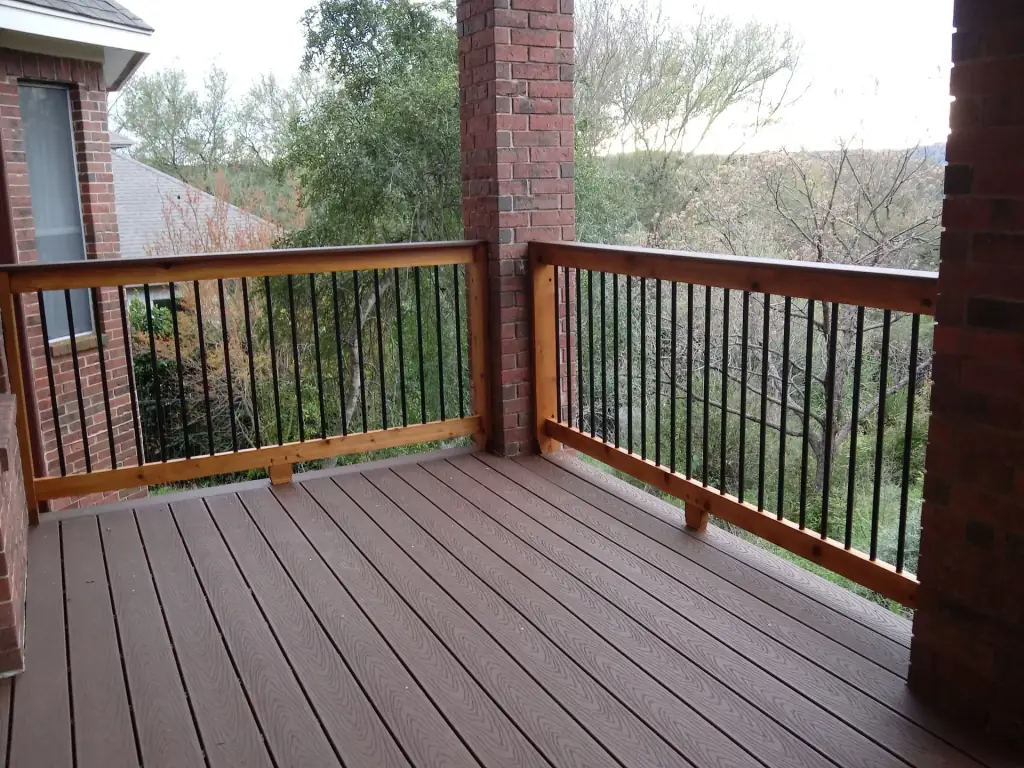 Upper level composite deck balcony with a cedar rail cap, black steel balusters and a Central Texas tree line view
