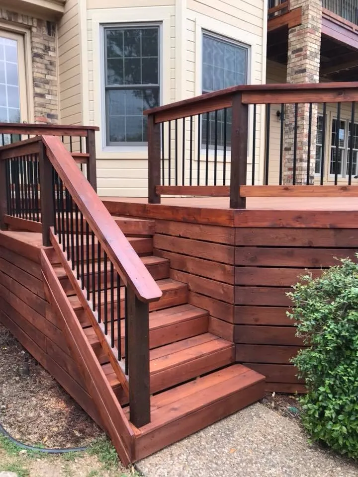 Mahogany stained deck stairs with black metal balusters against a two story home